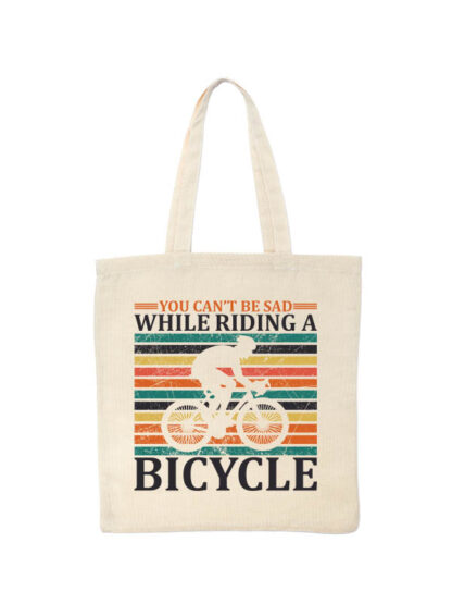 Ekotorba bawełniana w kolorze ecru z nadrukiem kolarza szosowego na tle kolorowych pasów. Całość opatrzona napisem You Can't Be Sad While Riding A Bicycle.